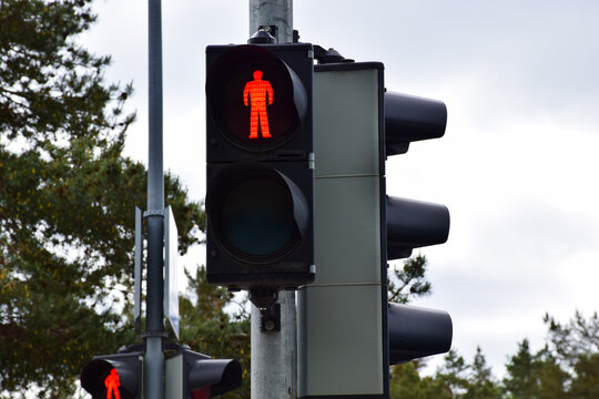 Red pedestrian traffic light showing stop signal on a metal pole against a cloudy sky in a city street