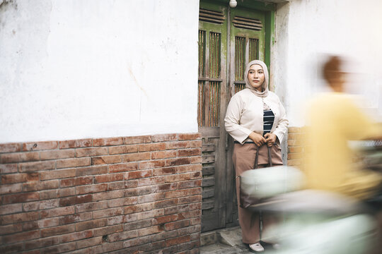 Asian Muslim Woman Standing Near Old Green Wooden Door as a Blurred Vehicle Passes By