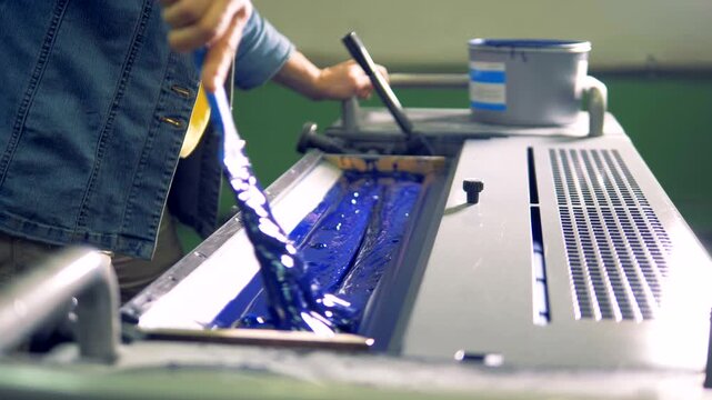 Printing worker spreading blue ink on a printing press