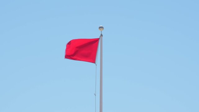Red Flag Warning Waving Against Blue Sky. Signaling Hazardous Swimming Conditions. USA Panhandle of Florida. No People. White Flag Pole Windy Wide.