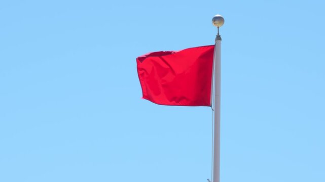 Red Flag Warning Waving Against Blue Sky. Signaling Hazardous Swimming Conditions. USA Panhandle of Florida. No People. White Pole Windy Closeup.