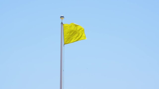 Yellow Flag Warning Waving Against Blue Sky. Signaling Hazardous Swimming Conditions. USA Panhandle of Florida. No People. White Pole Windy Wide.
