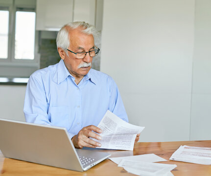 Senior couple checking bills and calculating expenses using a laptop at home, debt taxes concept, worried married elderly couple