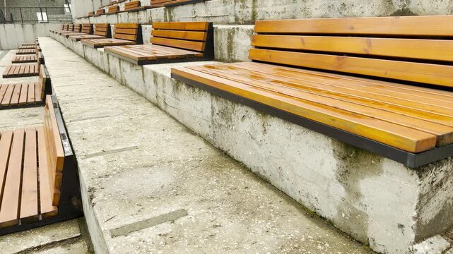 Polished wooden benches are mounted on tiered concrete steps. These rows form an open-air amphitheater that invites visitors to sit in this peaceful public setting.