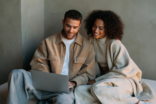 Couple using a laptop together on a couch in cozy neutral outfits for home lifestyle background and online browsing banner