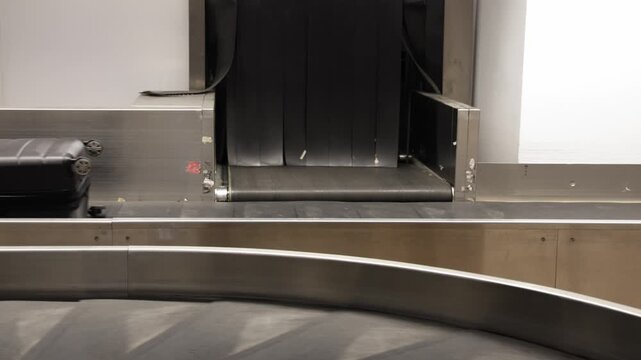 Black suitcase and polka dot bag arrive on baggage carousel, followed by a blue carry-on bag, showcasing the flow of luggage at an airport terminal