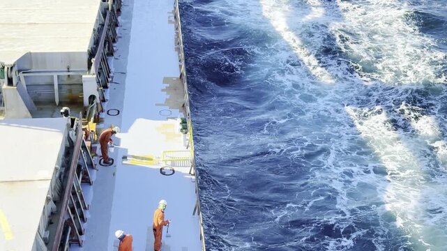 seafarer job on board during sea passage. moderate sea waves and crew working on deck. ship maintenance and painting near the ocean waves.