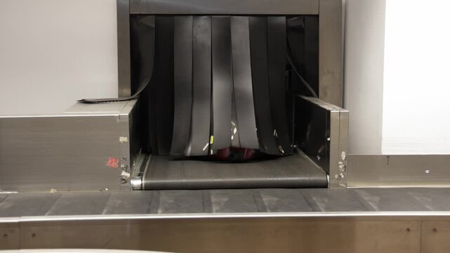 Luggage moving on conveyor belt at airport baggage claim, showing progression of blue suitcase entering and gray suitcase exiting the baggage area
