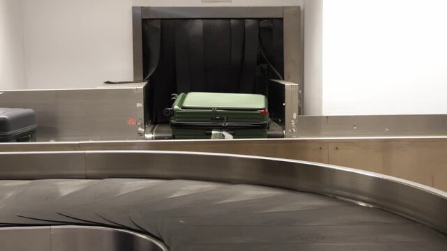 Luggage arriving on a baggage claim conveyor belt in an airport, showcasing a black suitcase followed by a purple suitcase and an empty area for additional bags
