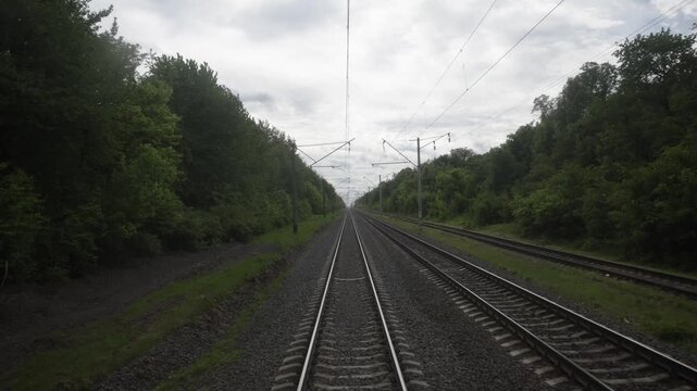 Train tracks stretching into the distance surrounded by lush greenery and trees on both sides, showcasing a serene landscape in a rural setting