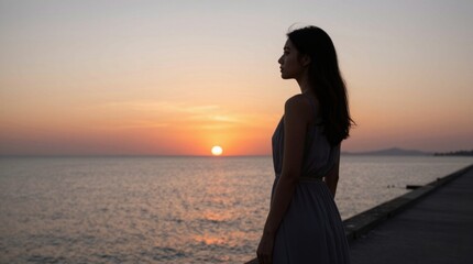 Fototapeta premium Woman standing watching sunset on seaside promenade