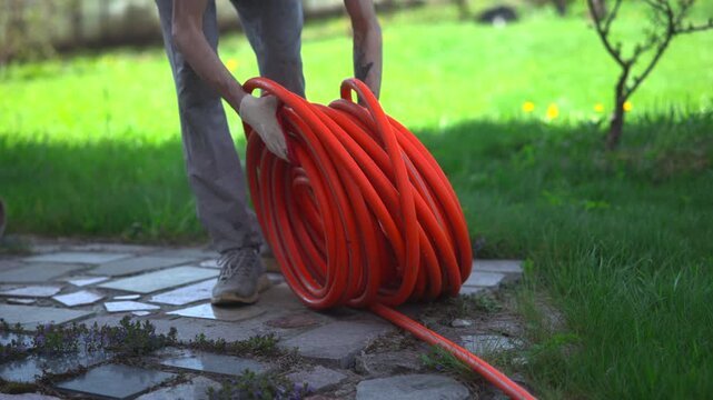 Person watering a backyard path with a coiled orange hose