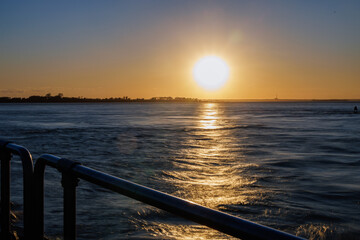 Obraz premium Sunset over water viewed past a waterfront railing