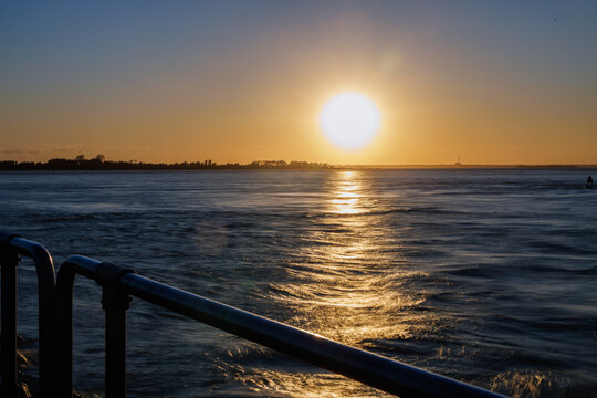 Sunset over water viewed past a waterfront railing