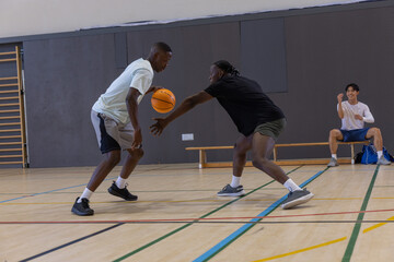 Diverse male friends playing basketball, dribbling, defending on gym court with orange ball © wavebreak3