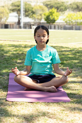 Fototapeta premium Female child sitting on purple yoga mat at park, wearing turquoise tee and navy shorts, meditating