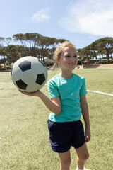 School-age girl standing on soccer field holding soccer ball balancing on left palm near line © wavebreak3