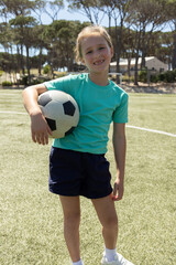 Obraz premium Girl child standing on grass pitch holding black-white soccer ball, wearing teal shirt, navy shorts
