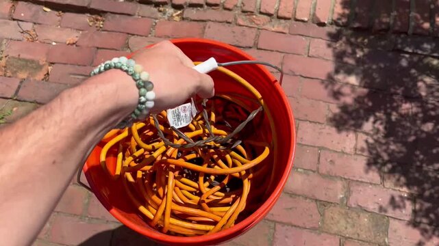 Man lifting and carrying orange bucket filled with extension cords