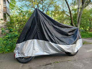 Motorbike covered with black and gray protective nylon parked in a residential courtyard close to a apartment building © Harmony Video Pro