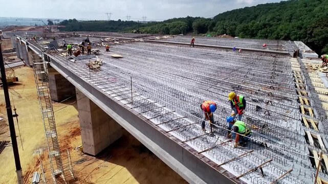 Workers installing steel reinforcement on a large concrete structure at a construction site, with formwork, scaffolding and crane support before concrete pouring.