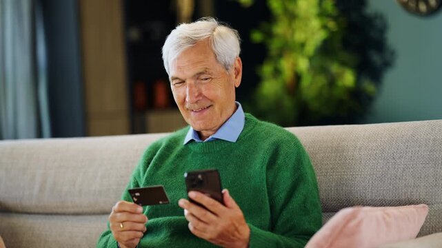 Elderly man using a smartphone and credit card to manage online payments and personal finances. Mobile banking, digital payments, fintech and financial independence.