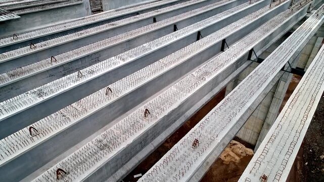 Aerial close-up of precast concrete beams stored at an infrastructure construction site, showing reinforced girder elements prepared for bridge, viaduct or road project assembly.