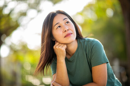Thoughtful Asian woman looking up while reflecting outdoors