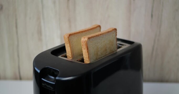 Bread slices popping up from toaster in kitchen during breakfast preparation. Vertical video captures morning routine, home cooking, simple meal preparation and fresh toasted bread ready to eat.