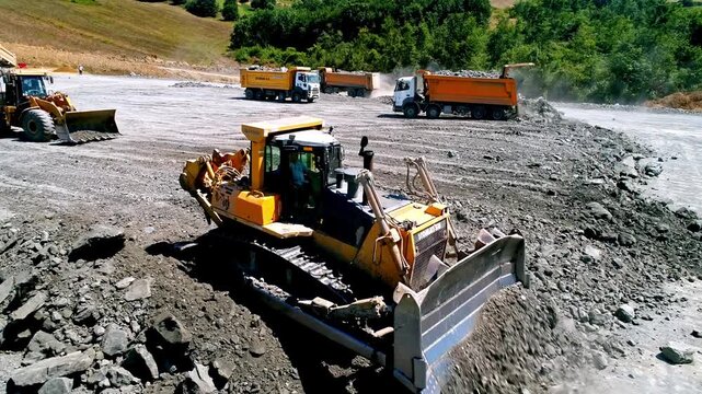 Dump truck unloading rock material at a large road construction site, with loaders, compactors and heavy machinery working on ground preparation and infrastructure development.