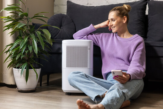 smiling woman sitting on the floor by air purifier at home. air quality and microclimate