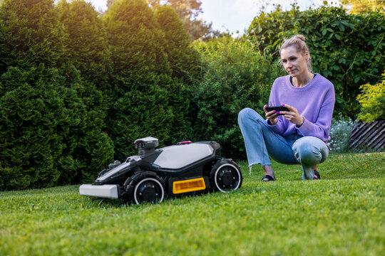 woman set up robotic lawn mower with smart phone at home garden
