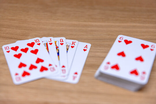Hand holding a playing card &mdash; six of hearts, card deck on table, gameplay moment
