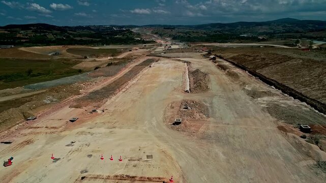 Aerial view of a rural highway construction site with paving machine, graded roadbed, earthworks and heavy equipment preparing a new transportation corridor.