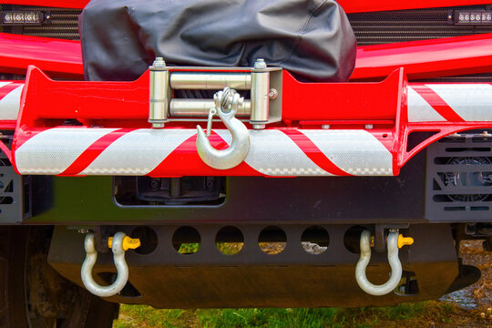 Close-up of a heavy-duty electric winch with a steel hook mounted on the front bumper of a red rescue vehicle.