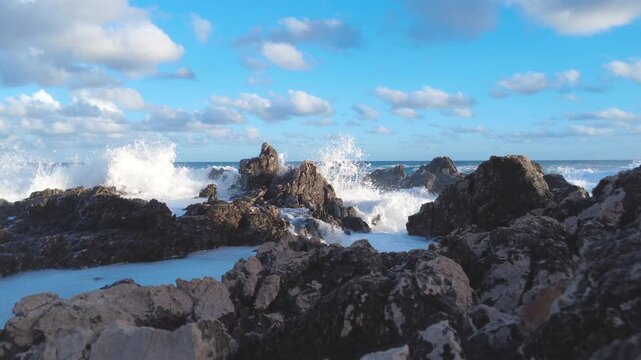 Dramatic sea waves smashing into black rocky shore on a sunny day. Rough ocean water splashing over stones, 4K ProRes video.