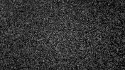 Fototapeta premium Close‑up of dark asphalt surface with embedded gravel and coarse texture, showing detailed irregular patterns and subtle variations in tone.