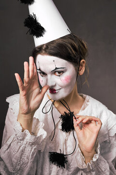 Playful woman in clown makeup gesturing thumb to nose holding hat string