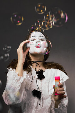 Woman in white clown makeup blowing soap bubbles from a pink bottle