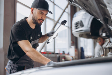 Fototapeta premium Mechanic inspecting car engine in service garage, performing maintenance during auto repair