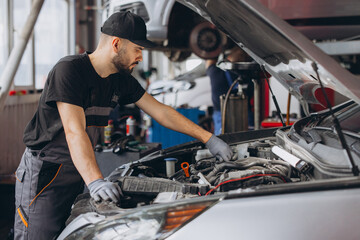 Fototapeta premium Mechanic checking car engine in auto repair shop, providing vehicle maintenance and diagnostic service