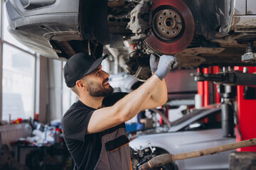 Mechanic man working on brake disc in auto repair shop, providing car service and maintenance © anatoliycherkas