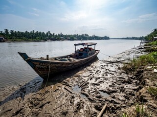 Obraz premium Weathered wooden fishing boat resting on a sun-drenched muddy riverbank at low tide in a wide-angle shot for authentic maritime and travel marketing