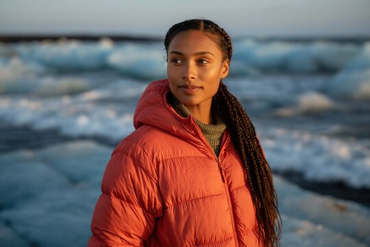 Woman wearing red puffer jacket standing by icy coastal waves