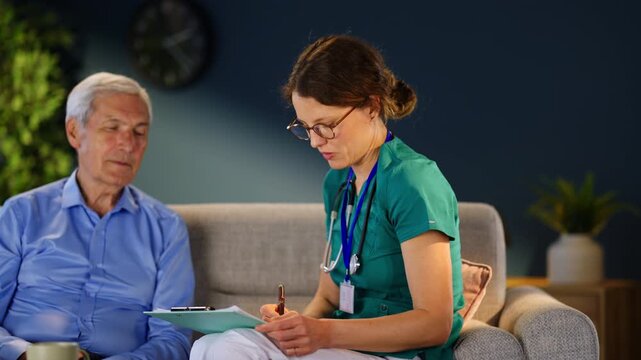 A nurse meets with a patient in a home setting. She listens to him while writing down important information. The meeting focuses on health and wellbeing.