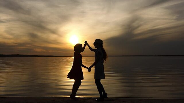 Two little sisters have taken up arms and are happily bouncing in front of the setting sun and the big lake. Beautiful sunset.