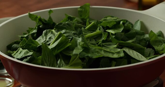 Concept home cooking and culinary inspiration. Tomatoes with are fried with green spinach leaves in a non-stick frying pan, the cook stirs the tomatoes with a wooden spatula.