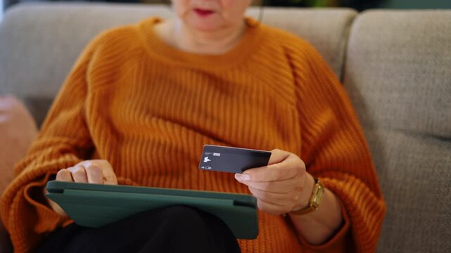 Elderly woman using a tablet and credit card for online shopping and digital payments. E-commerce, mobile banking, personal finance and technology adoption among seniors.