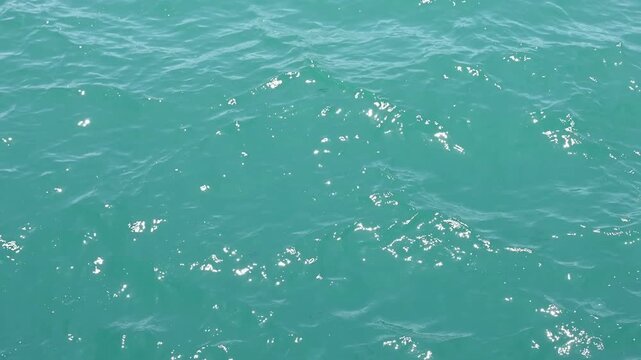Turquoise sea water surface with ripples and sun glint in summer. Clear ocean water wave high angle shot for tropical vacation and marine travel background.