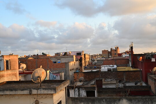 Rooftops of an old Moroccan medina with satellite dishes and distant mountains under a cloudy sky
